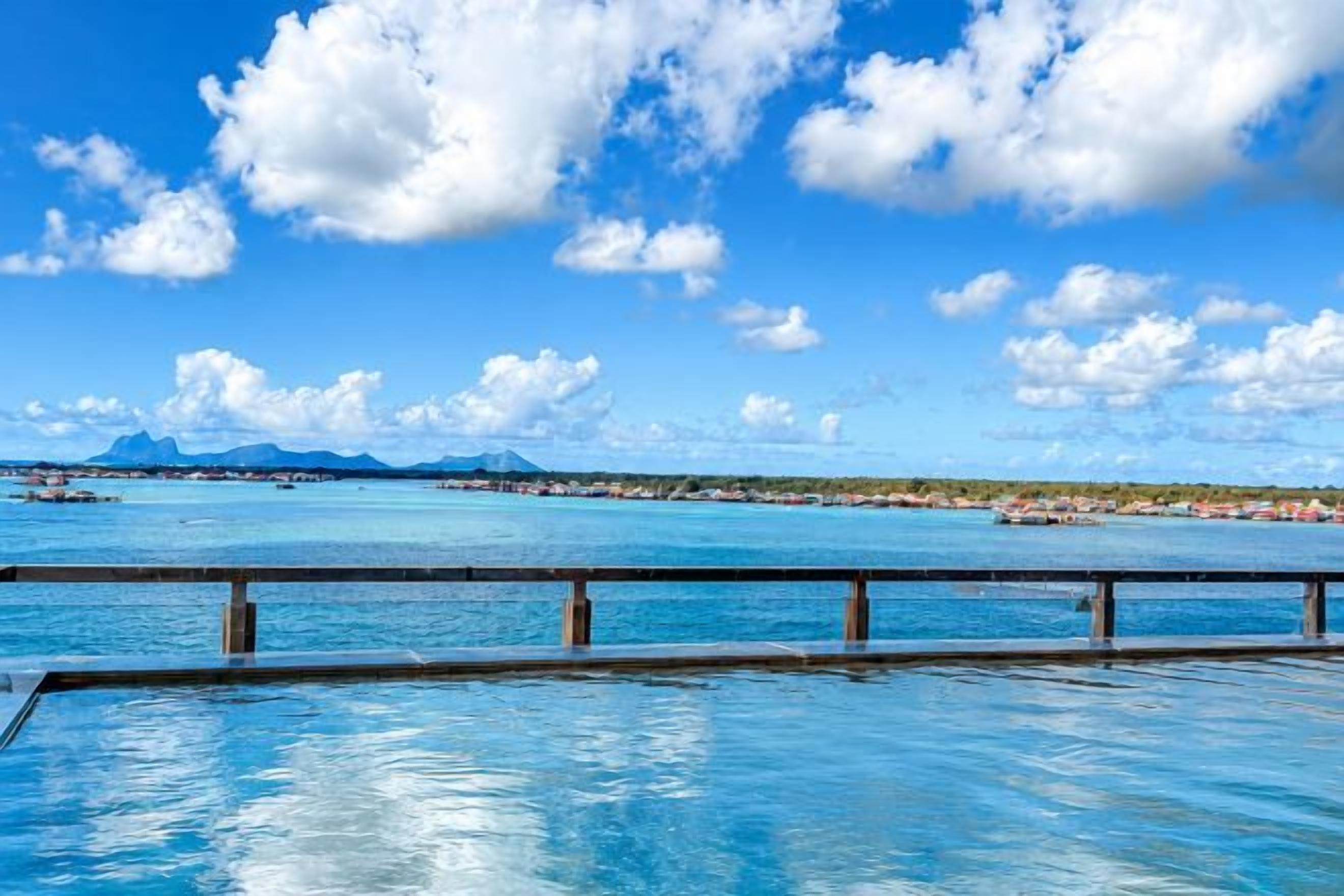 A swimming pool with a view of a tropical beach and distant mountains.