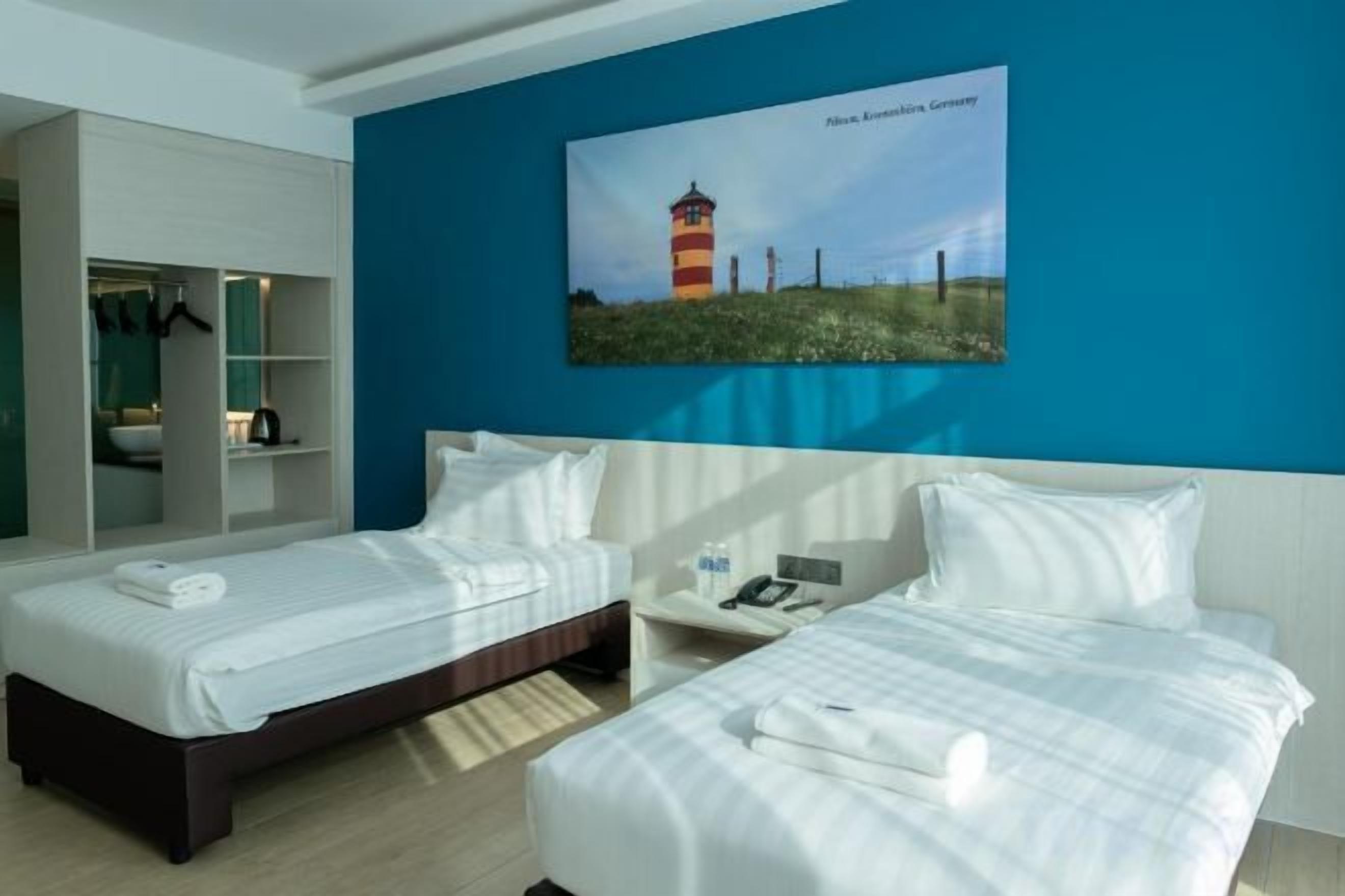 A hotel room with two beds, a wardrobe, a desk, and a painting of a lighthouse.