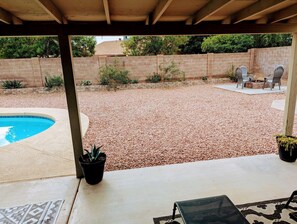 Ein überdachter Patio-Bereich mit Pool, Feuerstelle und Gartenmöbeln.