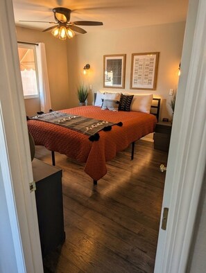 Ein Schlafzimmer mit einem Doppelbett, einem Deckenventilator und gerahmten Kunstwerken an der Wand.