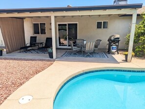 Ein überdachter Patio-Bereich mit Pool, Gartenmöbeln und Grill.