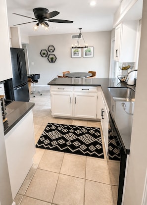 A modern kitchen with a black refrigerator, white cabinets, a round dining table, and a patterned rug.