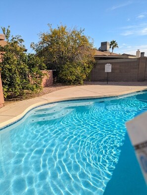 Una piscina con agua azul cristalina y bordeado de azulejos, rodeada por un muro de ladrillo y follaje.