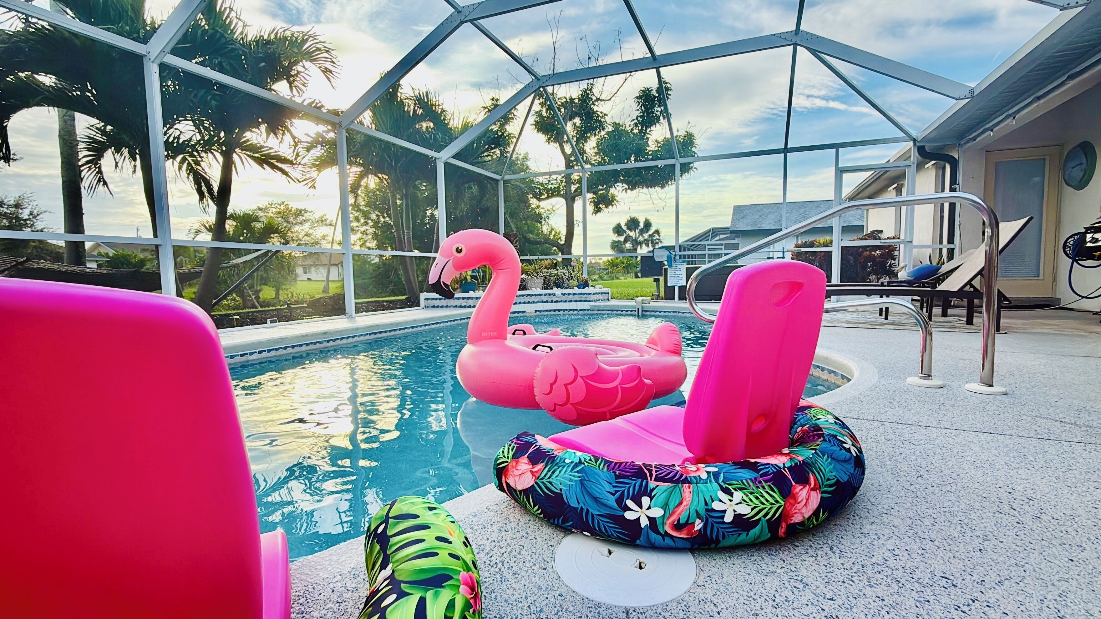 Ein Poolbereich mit einer gläsernen Struktur, einem Flamingo-Schwimmding und einem Lounge-Sessel im tropischen Stil.