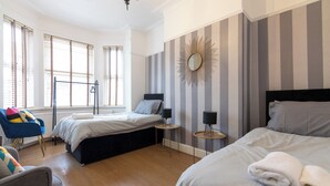 Une chambre d’hôtel avec deux lits, un coin salon avec un fauteuil, un miroir au mur et un radiateur.