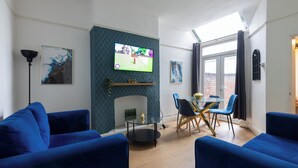 Un salon moderne doté d’une cheminée, d’un téléviseur à écran plat, de canapés bleus et d’un coin repas avec une table et des chaises en verre.
