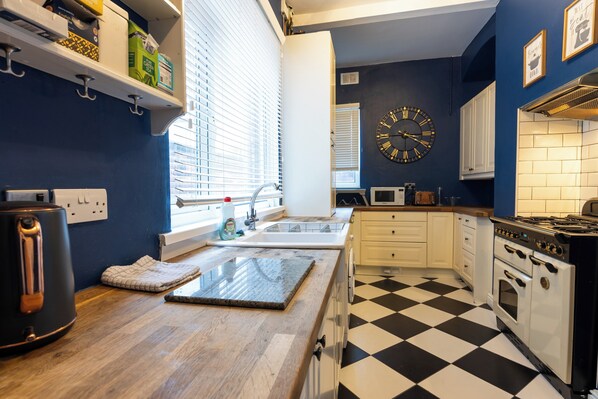 A kitchen with a black and white checkered floor, white cabinets, a stove, and a clock on the wall.