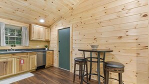 Ein Holzblockhaus-Innenraum mit Küchenzeile, einem Esstisch und Hockern sowie einer grünen Tür.