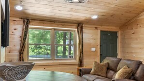 Ein Holzblockhaus-Interieur mit großem Fenster, einem Ledersofa und einer dekorativen Schale auf einem Tisch.