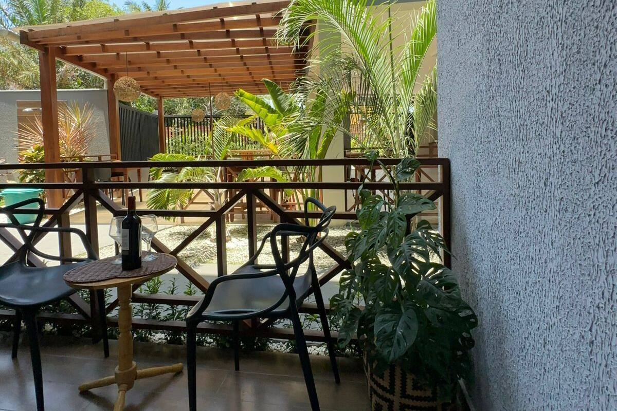 Un espace extérieur aménagé, abrité et doté d’une pergola, de chaises et d’une table sur laquelle se trouve une bouteille.