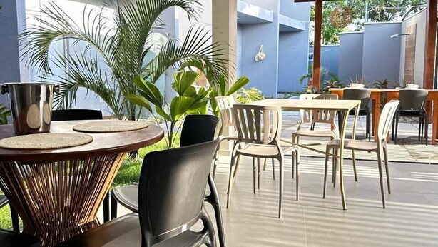 Un patio moderno al aire libre con mesas y sillas redondas, rodeado de plantas en macetas y una pérgola.