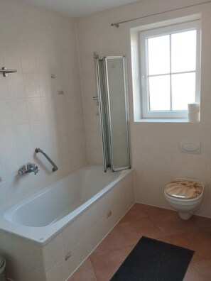 A bathroom with a bathtub, a toilet, and a window. - Vacation apartment Wechterswinkel (Bastheim)