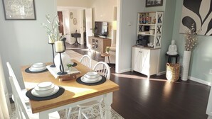Un comedor con una mesa de madera dispuesta para cuatro, sillas blancas y un aparador al fondo.