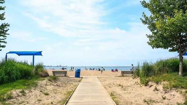 Una pasarela de madera que lleva a una playa con una toldería azul y bancos.