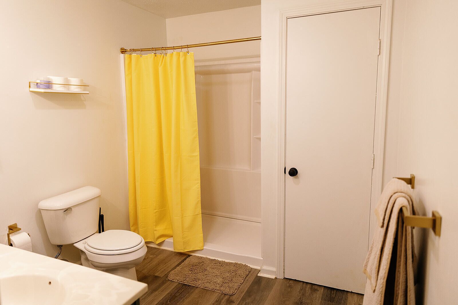 A bathroom with a toilet, a shower curtain, a towel rack, and a wooden floor.