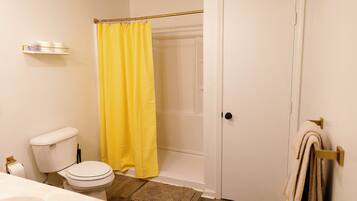 A bathroom with a toilet, a shower curtain, a towel rack, and a wooden floor.