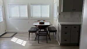A kitchen with a dining area, featuring a table with four chairs, a window with blinds, and a cabinet with drawers. - Charming 3-bedroom house with WiFi, AC , TESLA Charger in tranquil Lincoln City (Lincoln City)