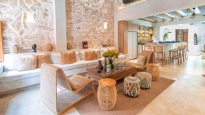Amplia sala de estar con pared de piedra, un conjunto de sofás, una mesa de centro y una cocina al fondo.