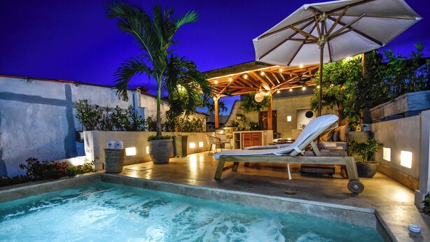 Un área de piscina con hidromasaje, sillones de descanso y sombrillas.