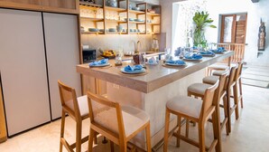 Una cocina con una isla central, taburetes de bar y estantes con vajilla y copas.