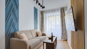 Ein modernes Wohnzimmer mit einer Couch, einem kleinen Tisch mit Flasche und Gläsern sowie einem an der Wand montierten Fernseher.