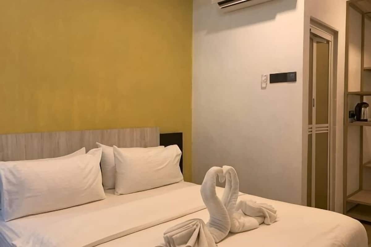 A hotel room with a bed, pillows, a towel, a door, and a wall-mounted air conditioner.