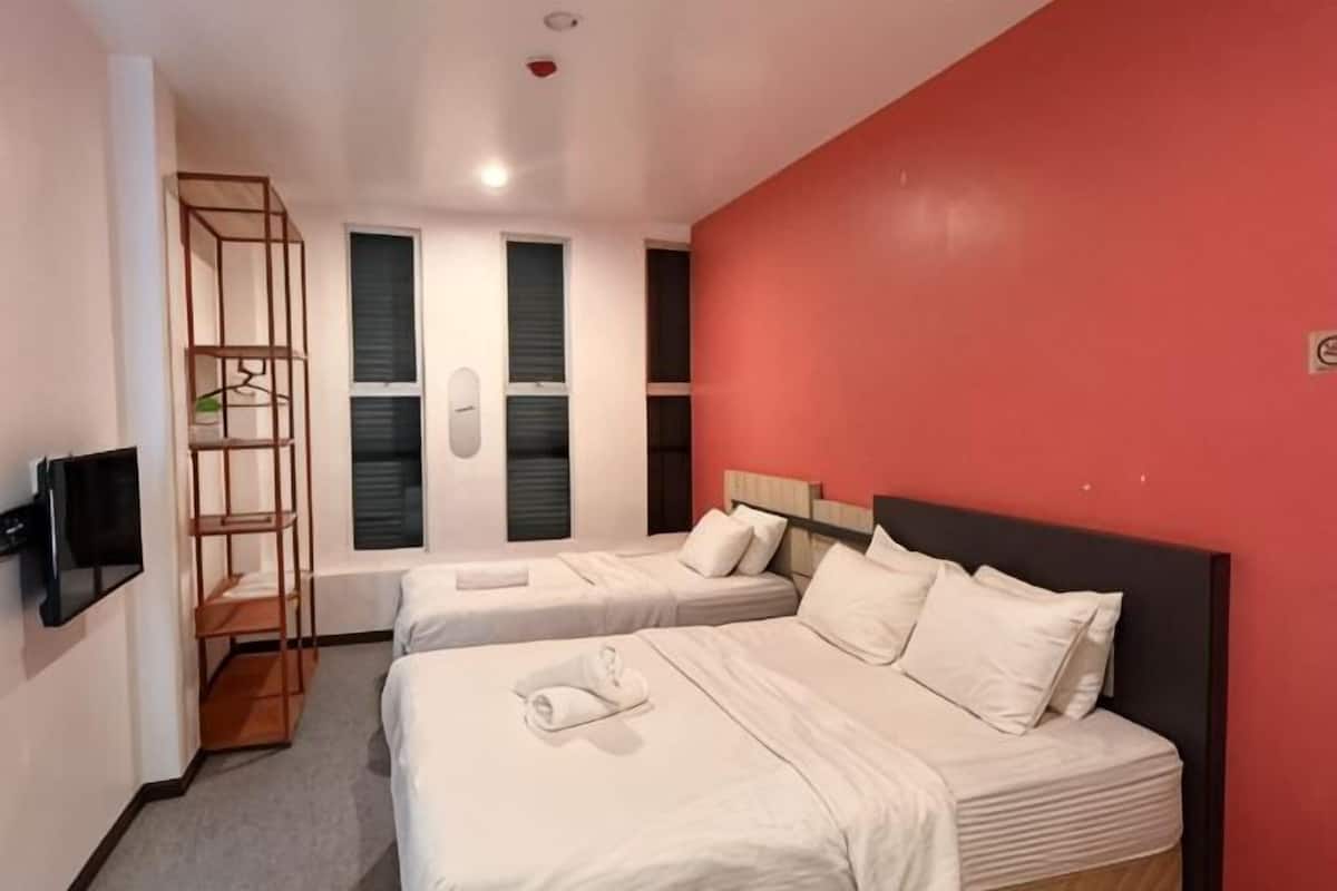 A hotel room with two beds, a TV, a wooden shelf, and a red accent wall.