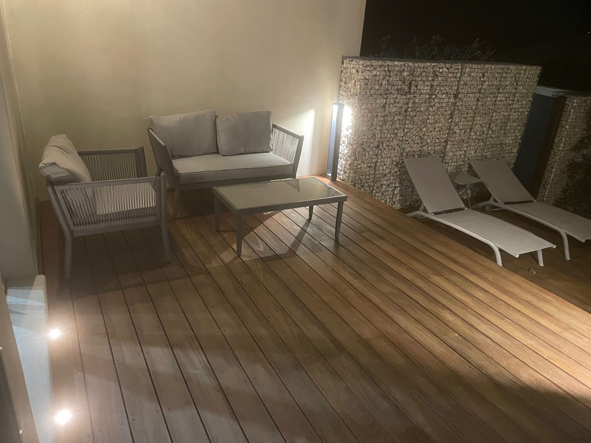 Une terrasse extérieure avec un plancher en bois, un canapé, une table et deux fauteuils.