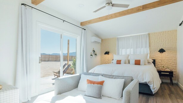 Een slaapkamer met een groot bed, een bank, uitzicht op het strand en een plafondventilator.