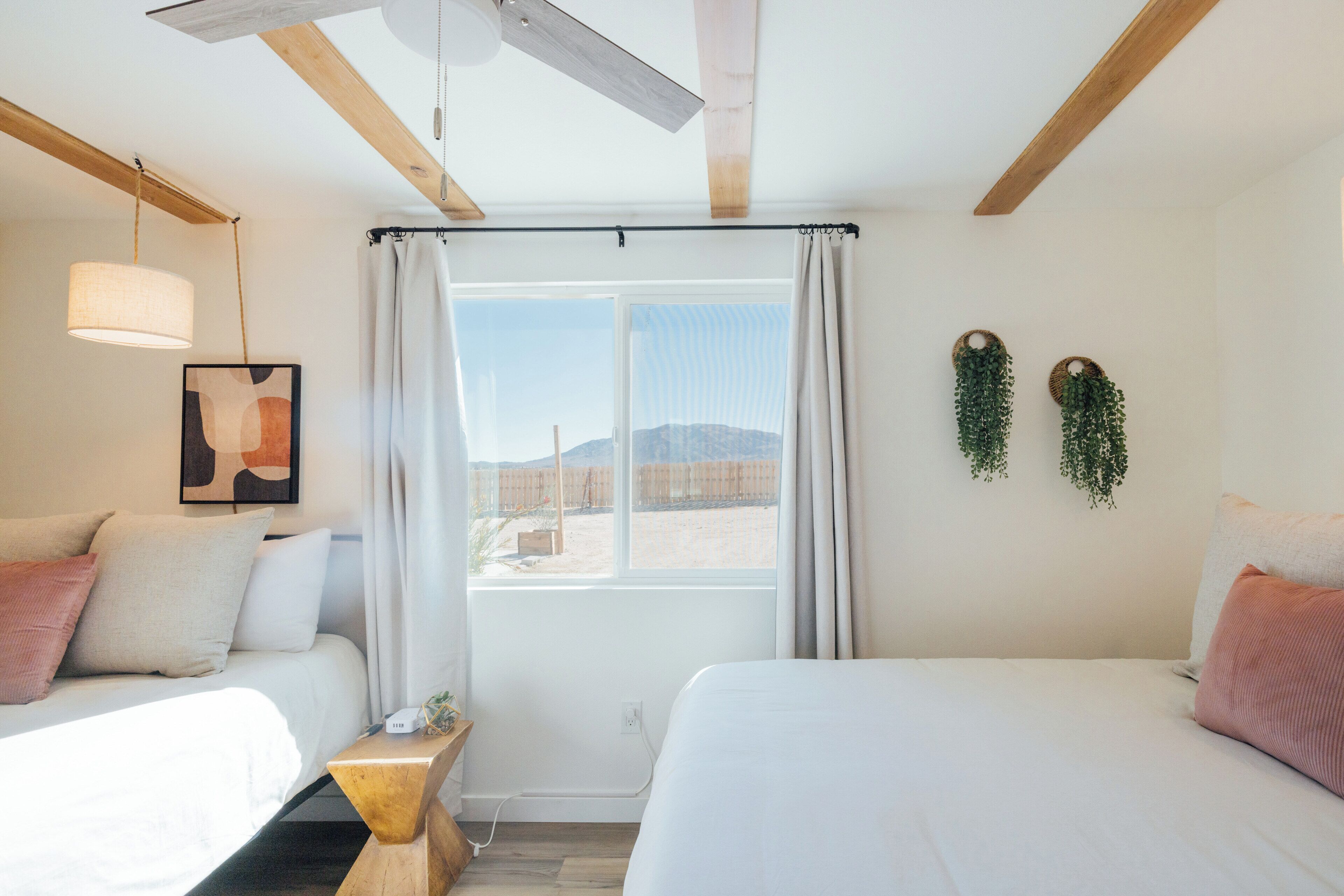 Habitació amb dos llits, una finestra amb cortines, un ventilador de sostre i una planta penjant a la paret.