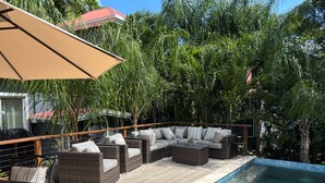 Uma área à beira da piscina com mobiliário de vime, piscina e vegetação exuberante.