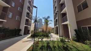 A multi-story residential building with balconies, a central courtyard with greenery, and a clear sky.