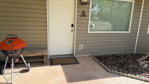 A house with a white door, a barbecue grill, a welcome mat, a lantern, and a window.