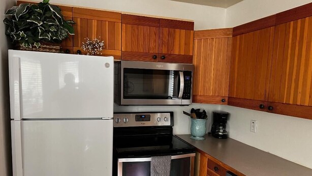 A kitchen with wooden cabinets, a white refrigerator, a microwave, an oven, and a coffee maker.