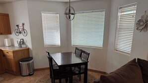 A dining area with a table and chairs, a trash can, a wooden cabinet, and a brown couch.