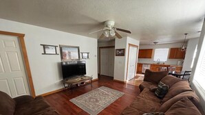 A living room with a brown sofa set, a flat-screen TV, and a ceiling fan.