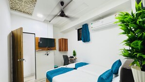 A modern bedroom with a bed, a television, a ceiling fan, and a potted plant. - Hotel Raksha Residency (Navi Mumbai)