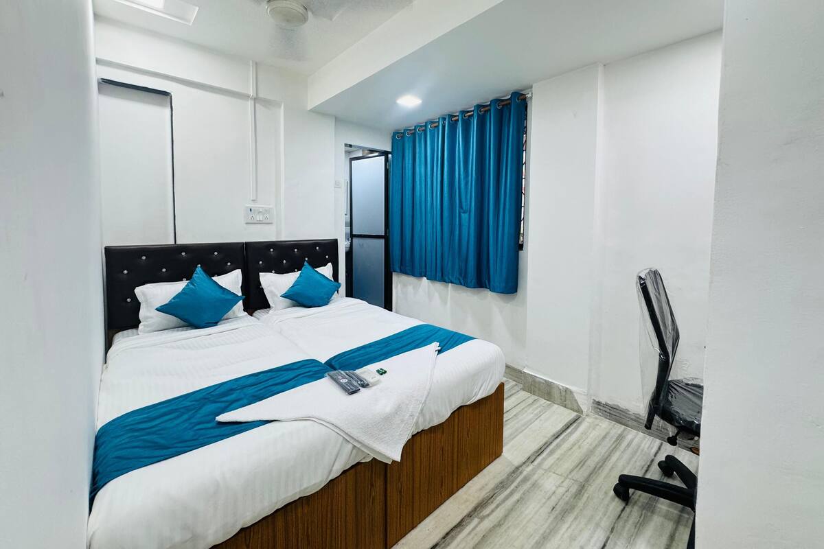 A neatly made bed with a white and blue bedspread, a wooden headboard, and a blue curtain on a window.