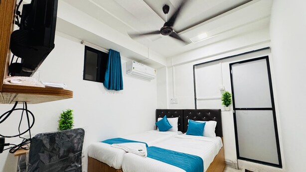 A modern bedroom with a bed, a ceiling fan, a TV, a small window, and an air conditioning unit. - Hotel Raksha Residency (Navi Mumbai)