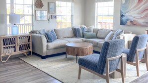 A modern living room with a sectional sofa, a round coffee table, and two blue armchairs. - Walk to beach, restaurants, & shopping. Charming, pet-friendly 3BR bungalow.  (Dauphin Island)