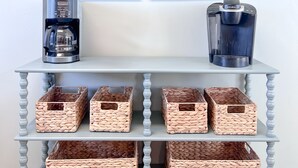 A room with a coffee station featuring two Keurig coffee makers, a wall-mounted sign spelling "Beach," and two framed paintings of a beach scene. - Walk to beach, restaurants, & shopping. Charming, pet-friendly 3BR bungalow.  (Dauphin Island)