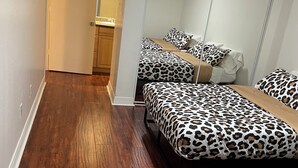 A hotel room with a wooden floor, two beds with leopard print bedding, a large mirror, and a door leading to a bathroom. - Lovely 2-bedroom condo in Phoenix with WiFi and AC (Phoenix)