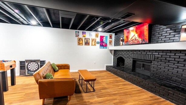A modern living room with a brick fireplace, wooden flooring, a sofa, a coffee table, and a dartboard.