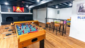 A room with a foosball table, a bar area with stools, a fireplace, and a wall with a poster.