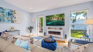 Uma sala de estar moderna com um sofá bege, um banquinho azul e uma televisão de tela plana montada acima de uma lareira.