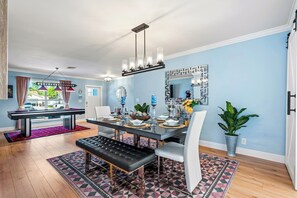 A dining area with a table set for four, a black leather bench, and a chandelier. - Heated Pool, Big Deck, Billiards, Games, PAC-MAN (Delray Beach)