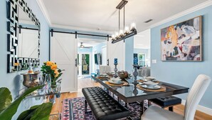 Uma área de jantar moderna com mesa de vidro, um banco estofado preto e cadeiras brancas.