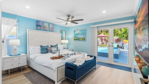 Quarto com cama, mesas de cabeceira, ventilador de teto e vista para a piscina e jardim.