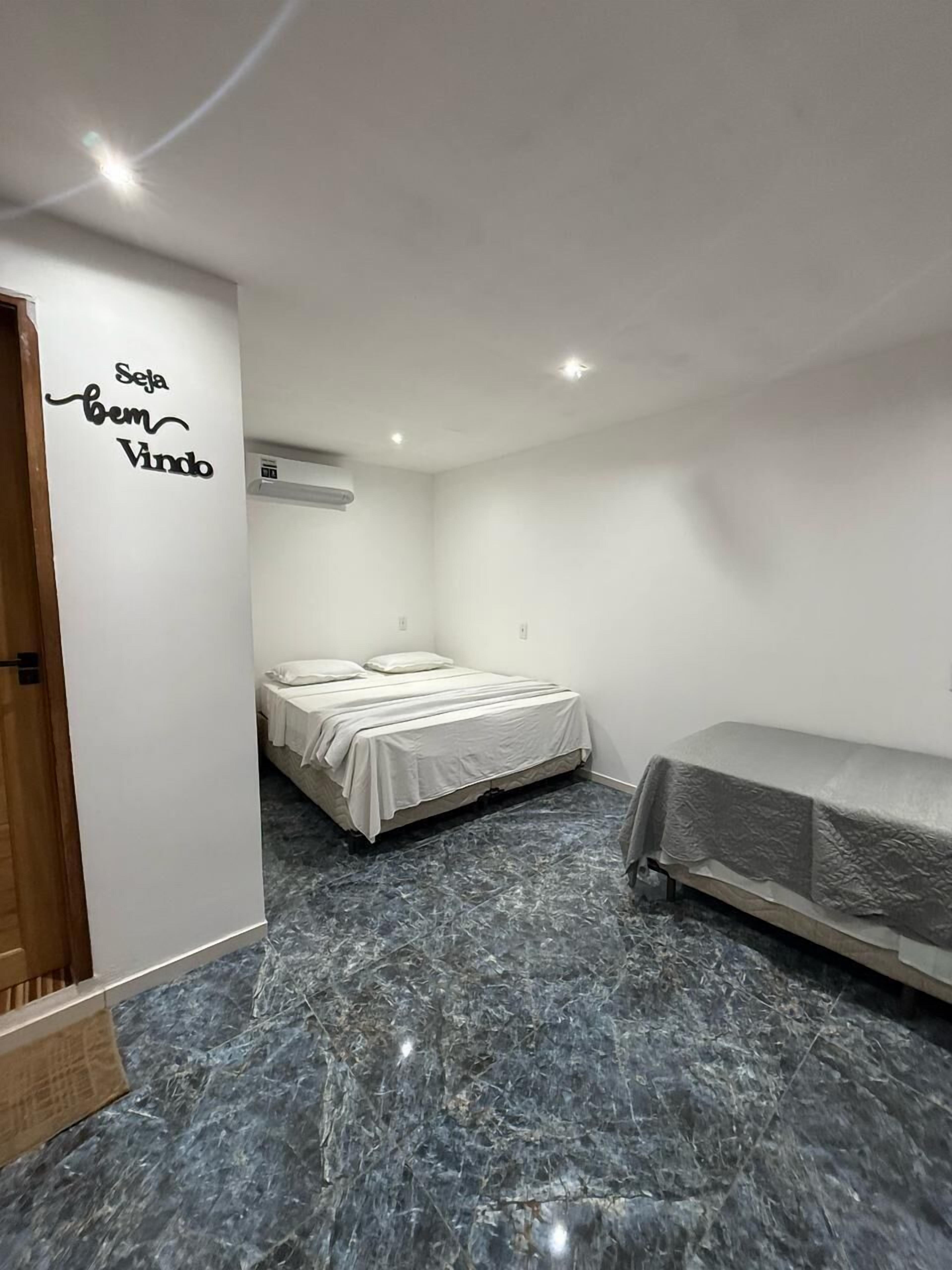 A bedroom with a bed, a bench, a wall-mounted air conditioner, and a marble floor.