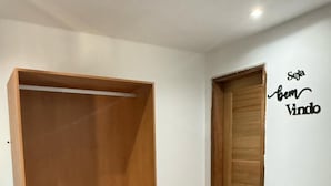 A room with a wooden wardrobe, a small white refrigerator, and a wooden door. - Pousada Visual de Noronha (Fernando de Noronha)